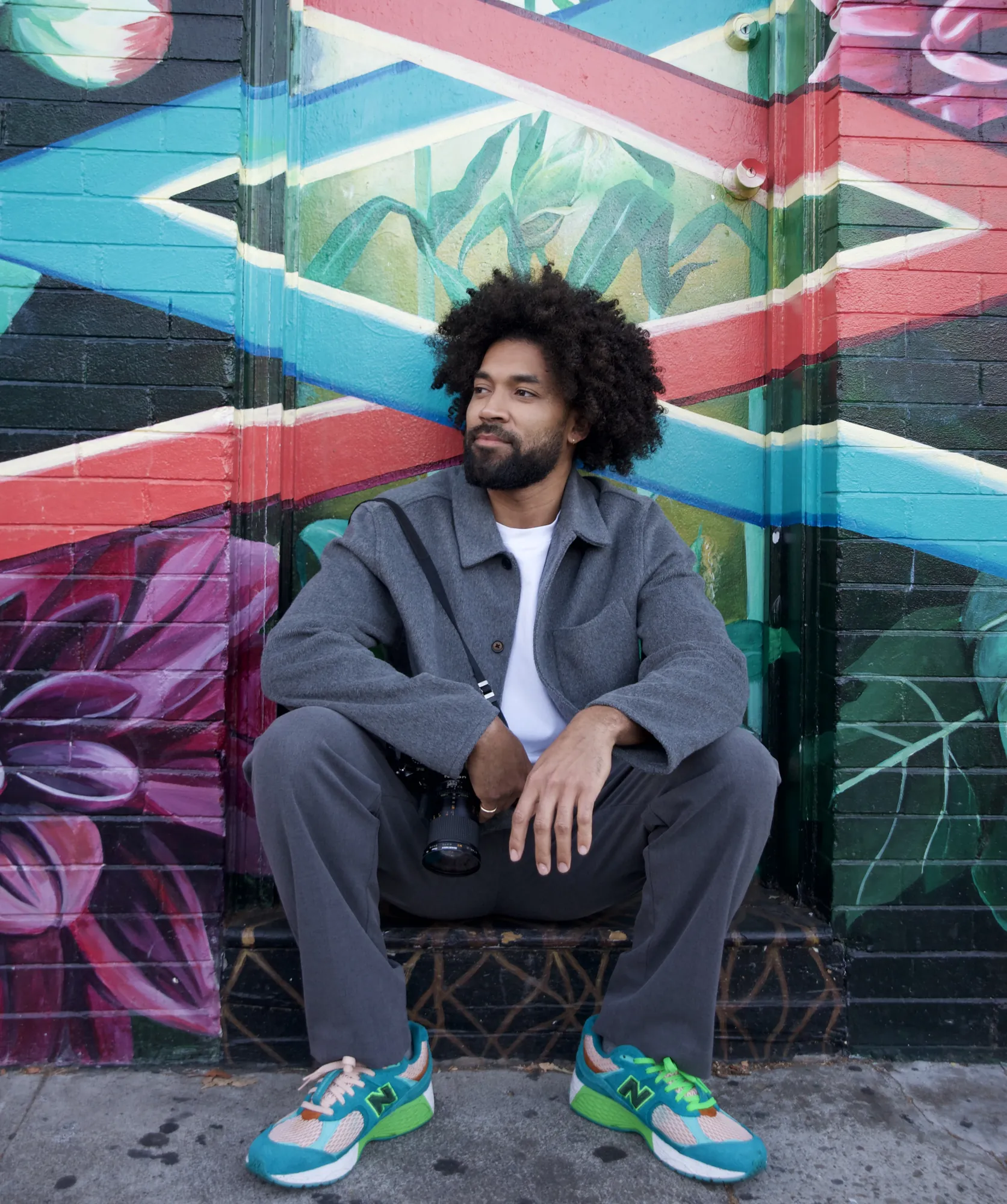 Man seated in front of a colorful mural wearing a grey overshirt
