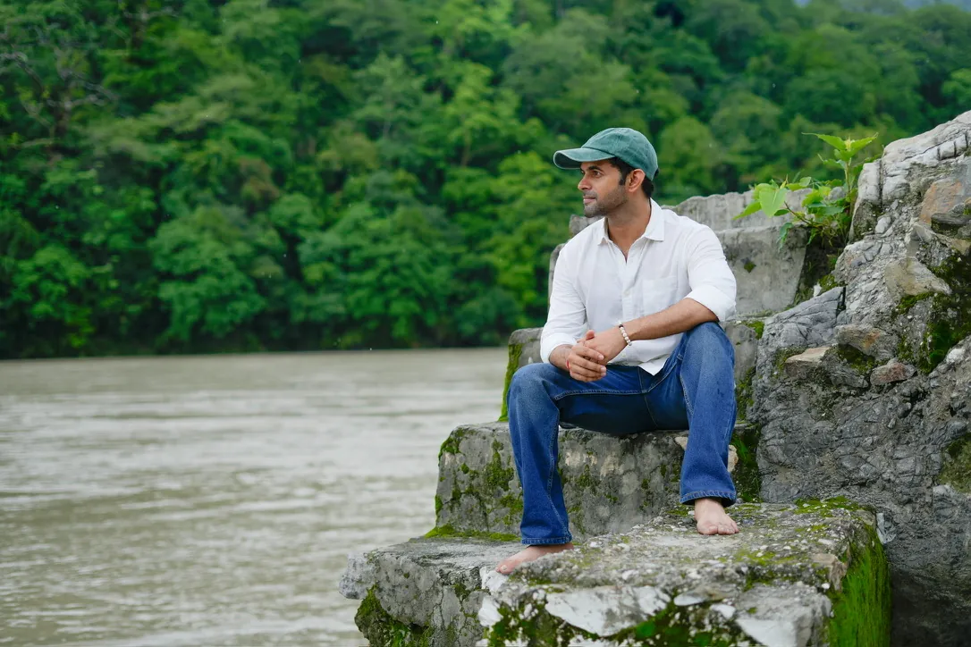 Man sitting barefoot on a mossy rock beside a river